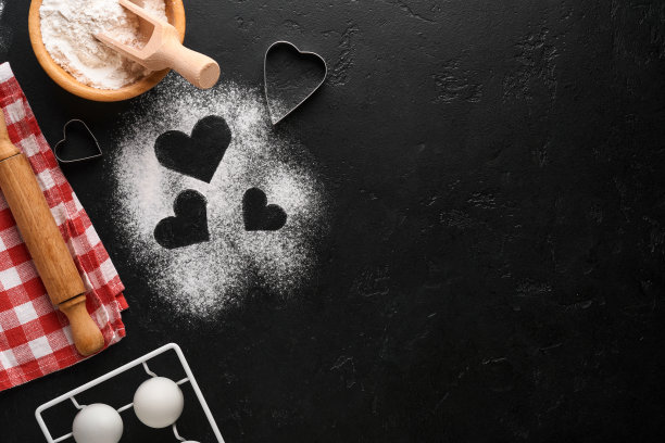 情人节烘烤背景与心脏形状，面粉，工具和配料自制饼干在黑色的桌子上。爱装饰食品背景。横幅。前视图。图片下载