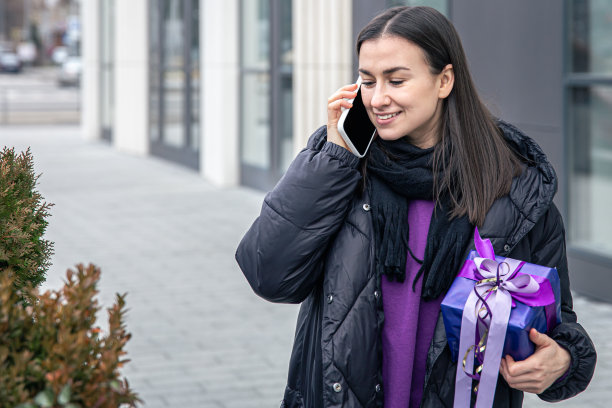 一个手里拿着紫色礼物的年轻女人在外面打电话。图片下载