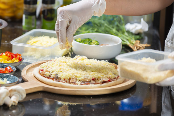 女人戴着手套，把马苏里拉奶酪涂在自制披萨的面团上。图片下载