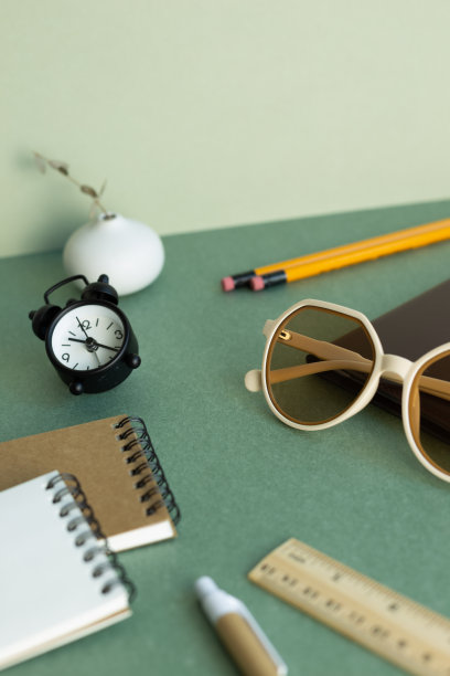 各种办公用品文具。笔记本，眼镜，铅笔，尺子，时钟，绿色桌面背景的植物图片下载