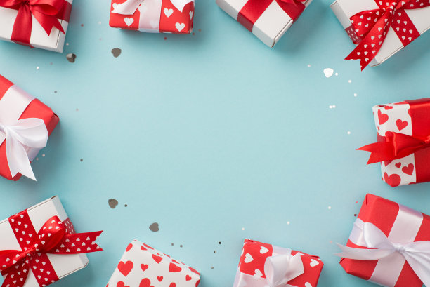 俯视图照片的情人节装饰心形纸屑亮片礼盒与心形图案的包装纸和蝴蝶结在孤立的淡蓝色背景与中间的空白图片下载