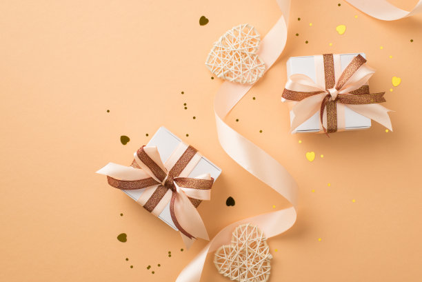 顶视图照片的情人节装饰白色礼盒与发光的棕色和浅米色蝴蝶结丝丝带藤心金色的五彩纸屑和亮片在孤立的米色背景copyspace图片下载