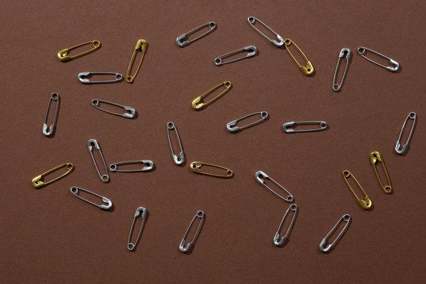 银色和金色的安全别针整齐地放置在深棕色背景的所有照片。副本的空间。模拟摄影。创意极简主义办公文具图片下载