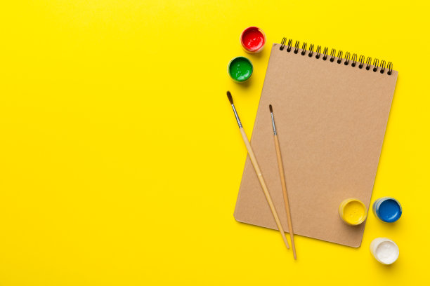 相册页和油漆，铅笔，画笔上的彩色背景。顶部视图与空的空间。工作场所的创造力。家庭教学概念图图片下载