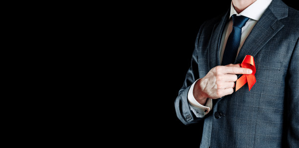 艾滋病。红丝带在世界艾滋病日孤立在黑暗的背景上。手持防癌用具和癌症标志的男子。健康,医学信号。副本的空间。图片下载