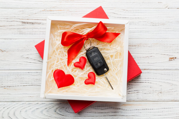 黑色汽车钥匙在一个礼物盒与丝带和红色的心在彩色背景。情人节作文俯视图图片下载