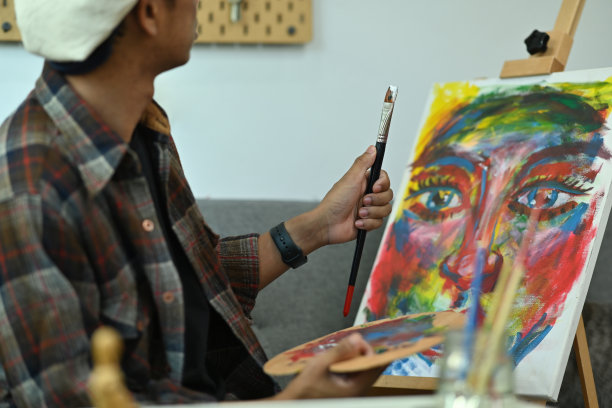 年轻有才华的男性艺术家在舒适的艺术工作室的画布上绘画的照片。图片下载