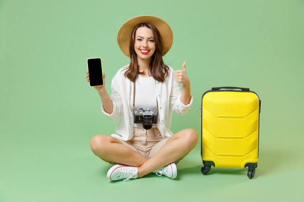 全身旅游的女人，便服，帽子，手提箱，使用手机，空白屏幕，坐显示像孤立在绿色背景上的乘客旅行国外周末航空飞行旅行概念。图片下载