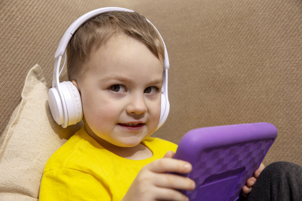 穿着黄色衬衫的快乐小男孩在家里玩平板电脑游戏。一个孩子在家里用紫罗兰色的平板电脑看卡通片的肖像。现代儿童教育技术。图片下载