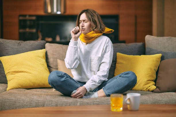 冷,感冒咳嗽。生病的女人坐在家里的沙发上咳嗽，喝着一杯热饮，一杯含有维生素c的药图片下载