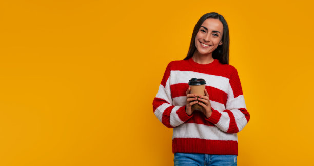 我的休息时间。可爱自信的现代黑发女人的特写肖像，而她摆姿势在工作室的黄色墙壁上的一些饮料的杯子图片下载