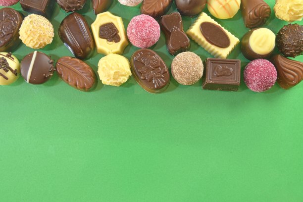 巧克力果仁框架顶视图库存图像。绿色背景上的巧克力糖果。巧克力框架顶视图。巧克力果仁背景与文本复制空间。不同糖果的边界图片下载