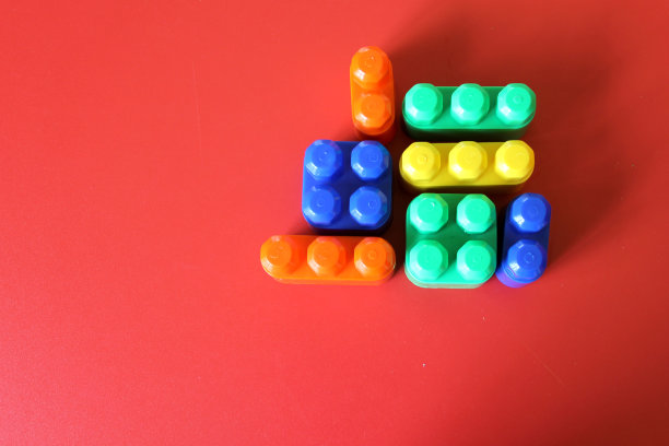 一块块五颜六色的塑料玩具积木形成并排列在红色的背景上图片下载