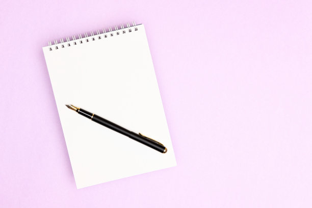 记事本，空白页和黑色钢笔在它的粉紫色背景图片下载