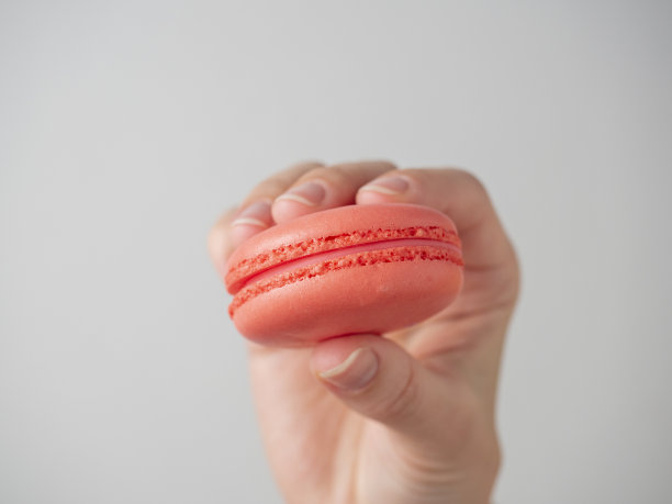 在白色的背景上，手拿橙色的甜马卡龙饼干。特写,空调产品图片下载