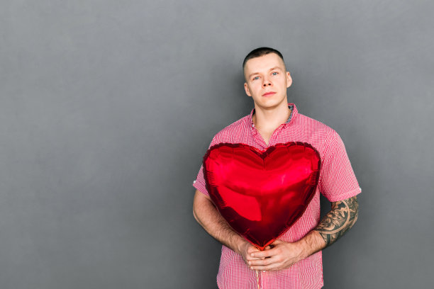 一个体格健壮的英俊男子手里拿着一颗红心。图片下载