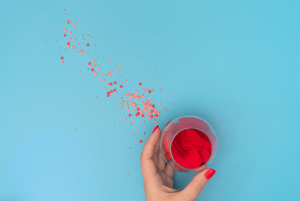 粉红色和红色的心与小珠子洒在女性手中的玻璃在蓝色的背景。贺卡。爱情，情人节或其他节日的概念。平面布局风格与复制空间图片下载