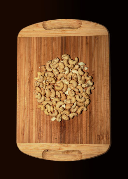 在木板上烤整颗腰果。用作点心的浅棕色坚果孤立的微距照片特写从上面的黑色背景。图片下载