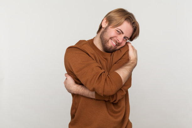 留着胡子的男人站着拥抱自己，露出露齿的微笑享受着积极的自尊。图片下载