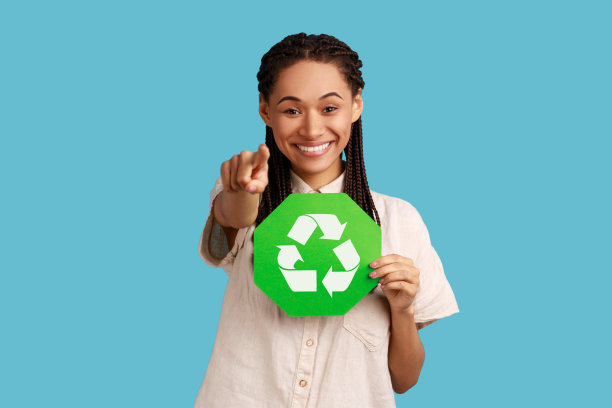 一名女子手里拿着绿色回收标志，手指着相机，想着绿色。图片下载