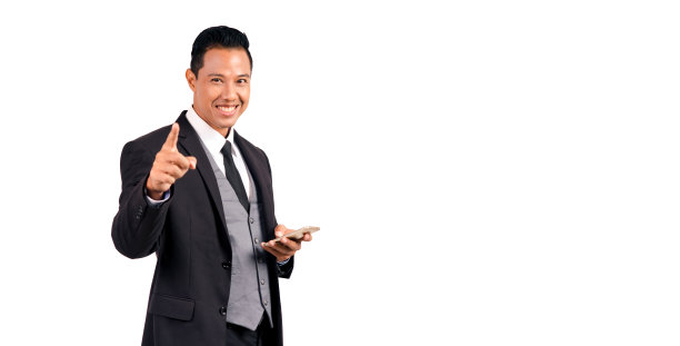 人像亚洲英俊的男子在西装拿着智能手机，手指指着相机在白色背景。图片下载