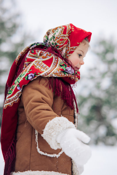 美丽的小女孩戴着红色的头巾走在白雪覆盖的森林里。图片下载