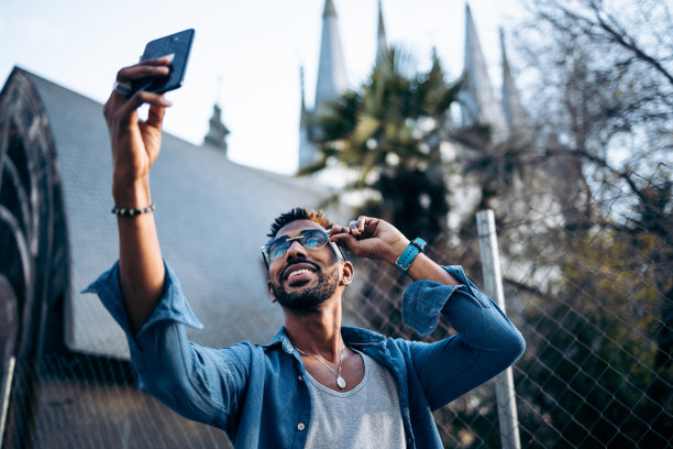 有型的非洲裔美国人，戴着眼镜，在街上用智能手机自拍图片下载