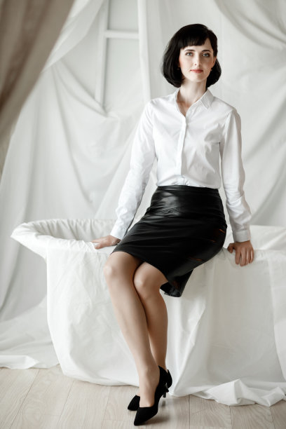 自信快乐有魅力的女商人。优雅的女孩穿着白衬衫和皮裙坐在家里的办公室图片下载