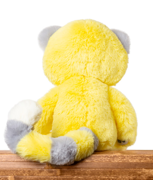 毛绒黄色玩具坐在一个木制的桌子上，与文字复制空间的特写后视图。图片下载