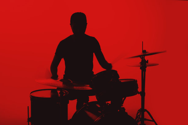 红色背景上打鼓的年轻男子剪影图片下载