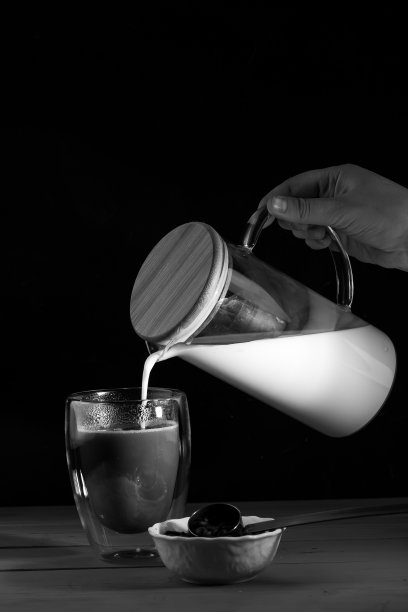 女孩把牛奶倒进有双层壁的杯子里。牛奶醒酒。木制桌子和黑色桌子。白色盘子里的咖啡豆。黑白照片图片下载