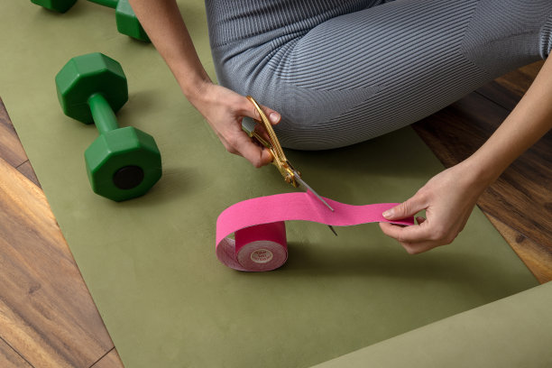 穿着运动服的女人坐在绿色的健身垫上，手里拿着剪刀和肌内效带。运动录制图片下载