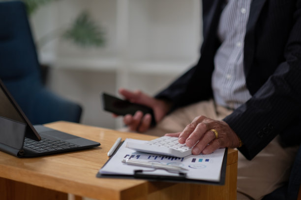 近在办公室使用计算器计算财务报表的老年会计的办公桌上的手。商人计算业务余额准备减税图片下载
