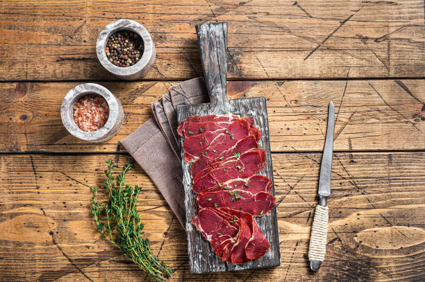 熏牛肉片，牛肉和香草放在木板上。木制背景。俯视图图片下载