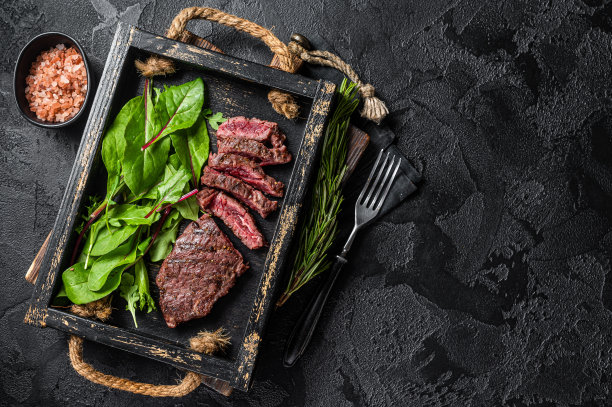 烧烤烤牛腩牛排在木制托盘与蔬菜沙拉。黑色背景。前视图。本空间图片下载