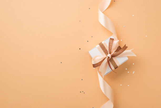俯视图照片的情人节装饰白色礼品盒与发光的棕色和浅米色丝带蝴蝶结和亮片在孤立的米色背景与空白空间图片下载
