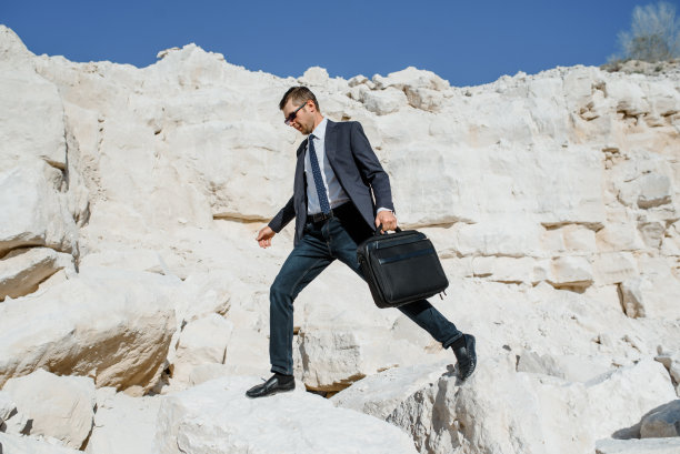 一个带公文包和夹克的年轻商人正在爬山。图片下载
