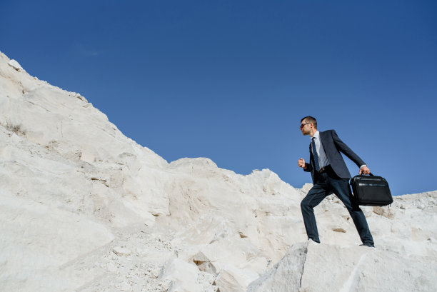 一个带公文包和夹克的年轻商人正在爬山。图片下载