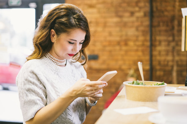 专注的女人在咖啡厅吃午饭时看手机。远程工作、社交网络滚动、聊天或做笔记。图片下载