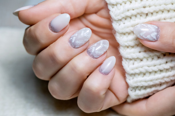 在指甲上画上白色的叶子和银色的闪光。女性冬季局部修甲。有创意的美甲图纸。新年的修指甲。美丽的女性指甲特写图片下载
