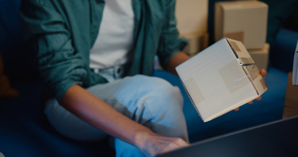 接近年轻的亚洲女售货员使用笔记本电脑在线商店准备运送到客户在家里晚上的包裹。图片下载