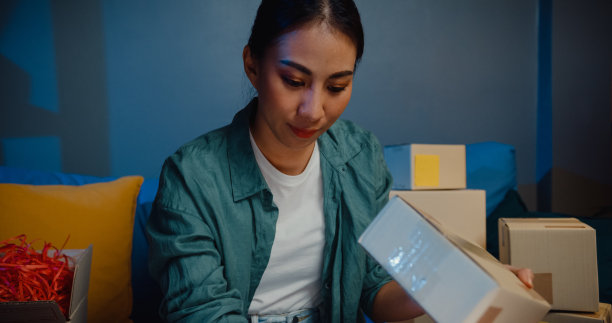 接近年轻的亚洲女售货员使用笔记本电脑在线商店准备运送到客户在家里晚上的包裹。图片下载