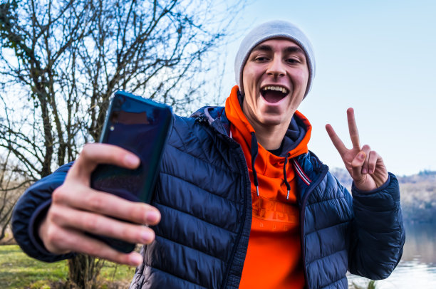 年轻的白人男子微笑着快乐地自拍，用手机自拍，看起来很兴奋，有乐趣，摆出酷的姿势，隔离在户外的通信技术概念图片下载