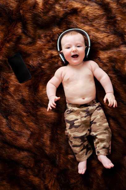 有趣快乐的小男孩用无线耳机在线听音乐，从他的手机。微笑的孩子正躺在耳机里，俯视图图片下载