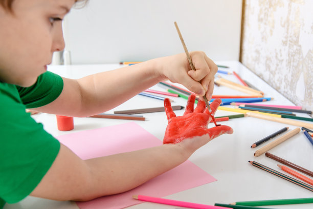 一个小男孩如何用红色颜料画他的手的特写。图片下载