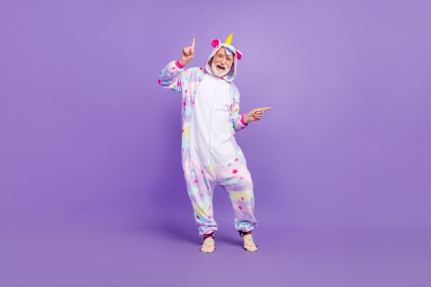 有趣的照片兴奋的男人养老金独角兽睡衣指着手指空空间跳舞微笑孤立的紫色背景图片下载