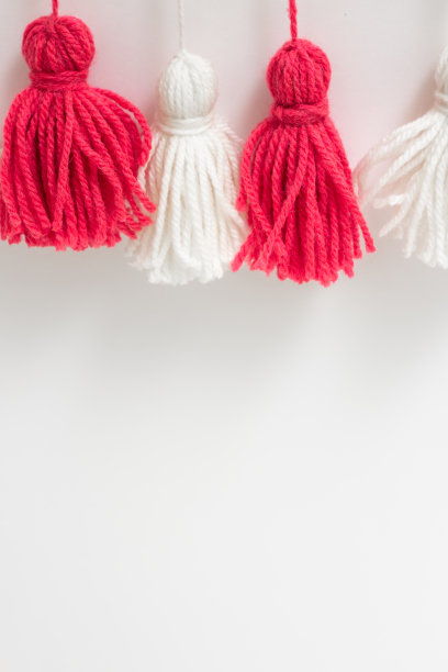 在白色的背景上用红色和白色的纱线制成的毛笔。DIY纱刷子。花环。纱的花环。Pampushki纱。孩子们的创造力。关闭计划。图片下载