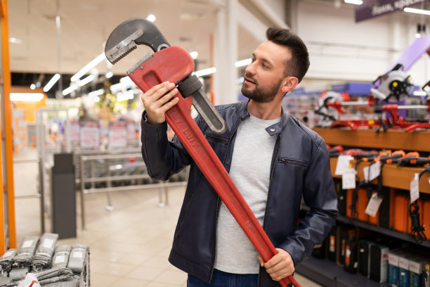 一名满意的男性买家在五金店，手里拿着一个巨大的红色扳手，脸上带着微笑图片下载