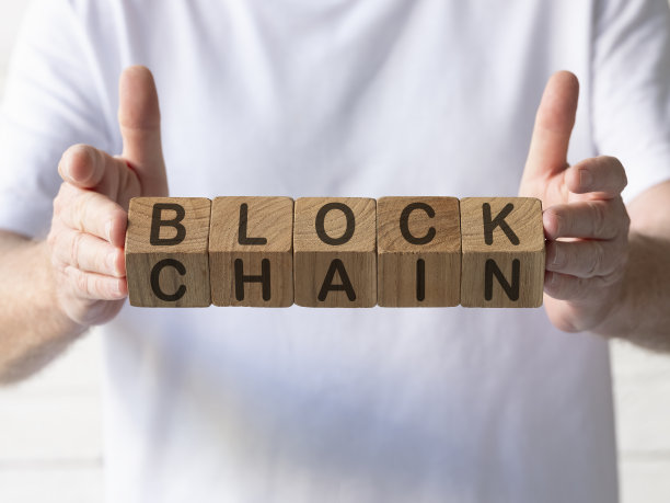 一名男子举着天然柚木木块，木块的两个角度上写着“区块链”。图片下载