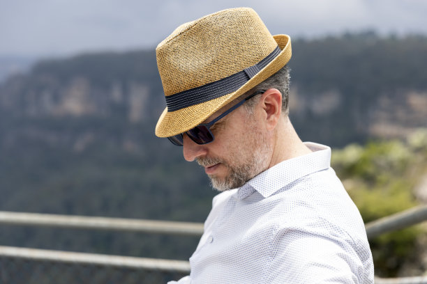 成年男子的肖像，戴着草帽，坐在户外向下看，背景与复制空间图片下载